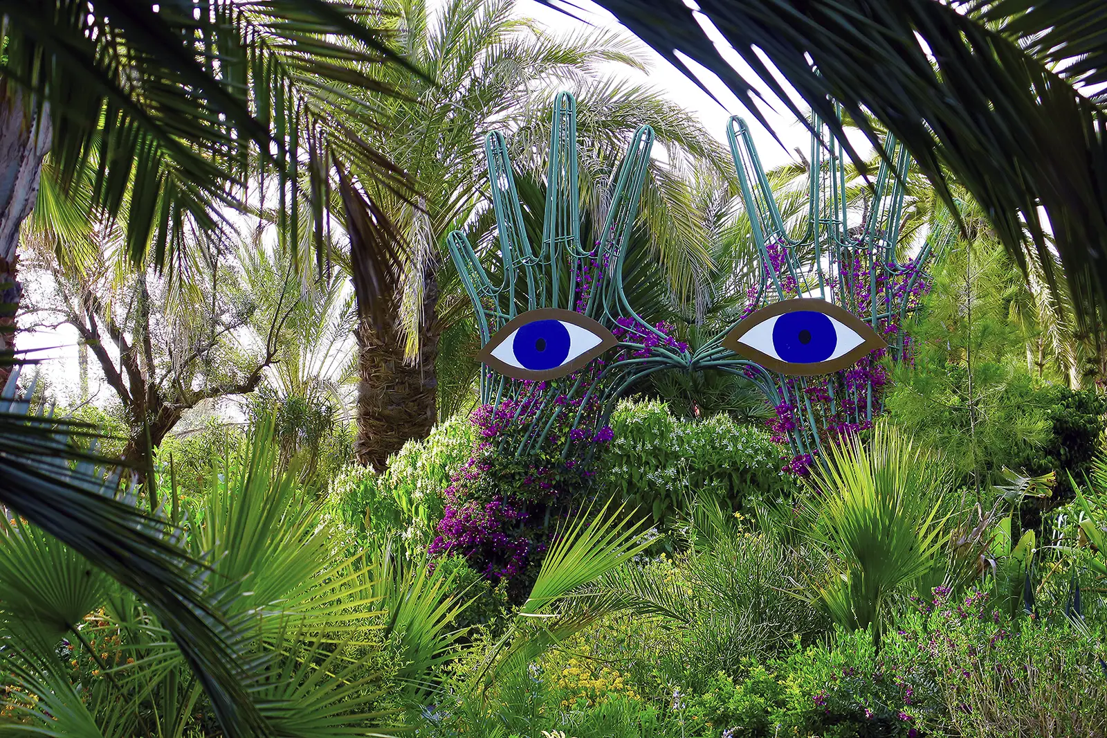 Une sculpture de visage aux yeux bleus au milieu des palmiers d'Anima Garden